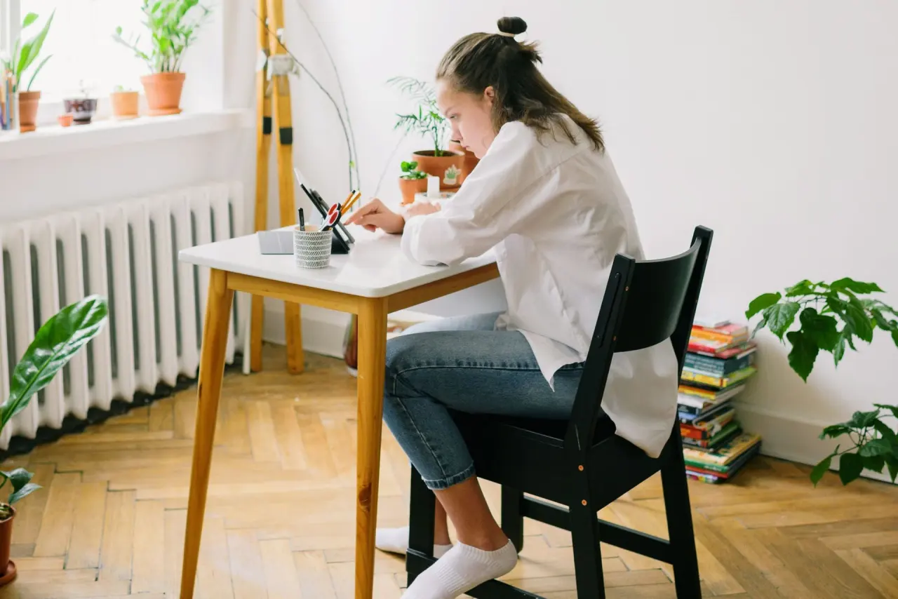 Une adolescente installée à son bureau devant une tablette, dans une chambre lumineuse